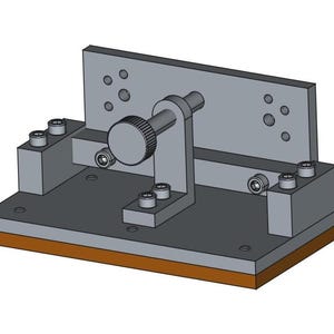 Könnte beinhalten: Eine mechanische Vorrichtung mit einem grauen Metallrahmen, die einen Drehknopf und mehrere Schrauben aufweist. Die Basis hat einen braunen Rand. Das Design scheint für industrielle oder technische Anwendungen bestimmt zu sein.