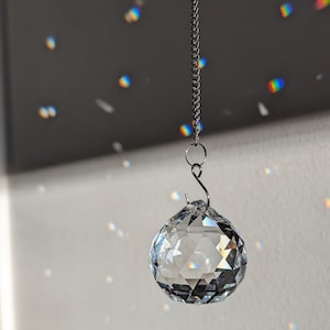 May include: A clear crystal ball hanging from a silver chain. The ball is faceted and reflects light.
