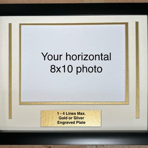 May include: Black picture frame with a gold mat and a white background. The frame is designed to hold an 8x10 inch horizontal photo. The text "Your horizontal 8x10 photo" is printed on the white background. A gold plaque with the text "1-4 Lines Max. Gold or Silver Engraved Plate" is at the bottom of the frame.
