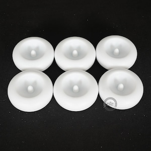 Pode incluir: Seis objetos circulares brancos com uma caracter&iacute;stica cil&iacute;ndrica central elevada. Os objetos est&atilde;o dispostos em duas filas de tr&ecirc;s contra um fundo escuro. Os objetos parecem ser feitos de um material liso e opaco.