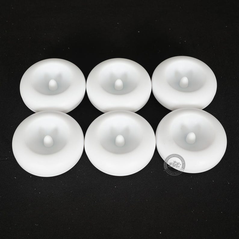 Pode incluir: Seis objetos circulares brancos com uma caracter&iacute;stica cil&iacute;ndrica central elevada. Os objetos est&atilde;o dispostos em duas filas de tr&ecirc;s contra um fundo escuro. Os objetos parecem ser feitos de um material liso e opaco.