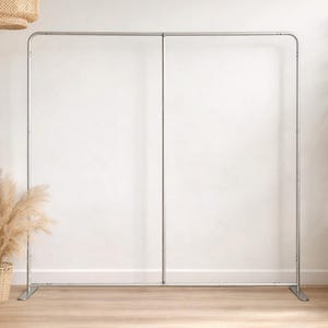 May include: A silver metal backdrop stand with a rectangular frame. The stand has a vertical center support and is set against a white wall. The stand is designed for events and photography.