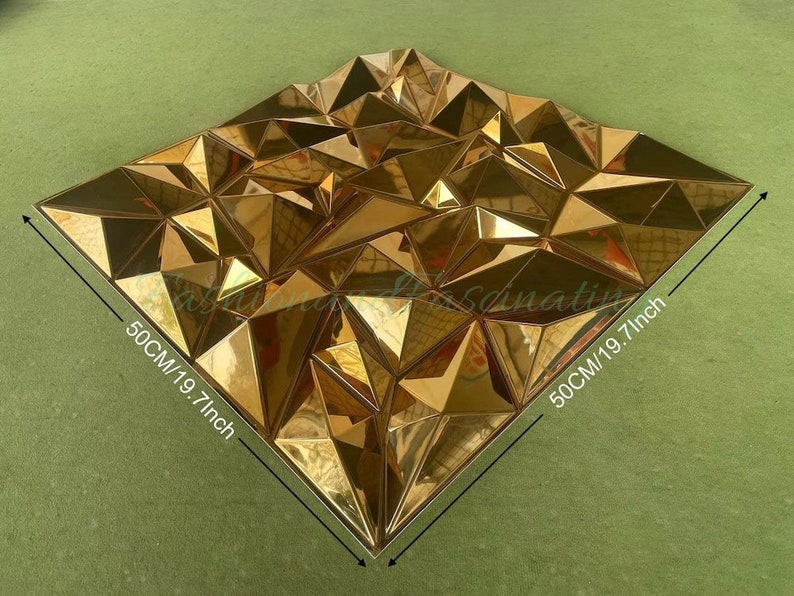 May include: Gold geometric wall panel with a 3D design. The panel measures 19.7 inches by 19.7 inches.