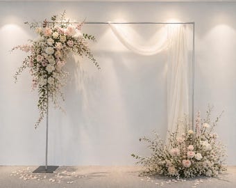 Könnte beinhalten: Ein rechteckiger Ständer aus silbernem Metall, dekoriert mit einem großen Gesteck aus weißen und blassrosa Rosen, Grünpflanzen und Schleierkraut auf der linken Seite, mit einem transparenten weißen Stoffvorhang und einem passenden Blumengesteck am Boden.