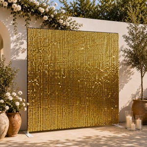 Op de afbeelding: Een groot, vierkant, vrijstaand achtergrondpaneel bedekt met reflecterende, metallic gouden lovertjes. Het paneel is gemonteerd op een dun zwart frame met witte voetsteunen, wat een glinsterend, rasterachtig oppervlak creëert dat het licht vangt.