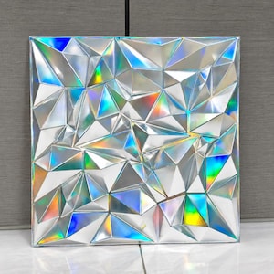 May include: A square wall panel featuring a three-dimensional geometric design composed of numerous triangular facets. The surface has a reflective, metallic silver finish that creates a holographic effect, displaying vibrant rainbow light refractions.