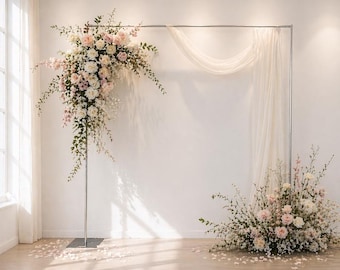 May include: A floral arch with a metal frame, adorned with white and pink flowers and greenery. A matching floral arrangement sits at the base. White fabric drapes from the top of the frame, creating a soft backdrop for a wedding or event.
