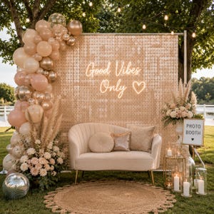 May include: A decorative outdoor event setup with a beige loveseat, sequin backdrop, and balloon arch. The backdrop features the text "Good Vibes Only" in neon. A "Photo Booth" sign and candles complete the scene.