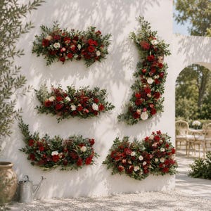 May include: Five floral arrangements of red and white roses and greenery are mounted on a white wall. The arrangements are in various shapes, including rectangular and curved designs. The scene is outdoors with a neutral background.