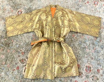 May include: Gold-colored kimono with a repeating circular pattern and an orange interior. The kimono has wide sleeves and a matching belt. The fabric has a subtle sheen, and the design is intricate.