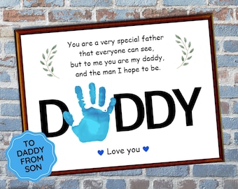 Op de afbeelding: Een ingelijst afdruk met een blauwe handafdruk en het woord "DDDY" in het zwart. De afdruk bevat de tekst "Je bent een hele speciale vader die iedereen kan zien, maar voor mij ben je mijn papa, en de man die ik hoop te zijn." De afdruk bevat ook de tekst "TO DADDY FROM SON" en "Love you".