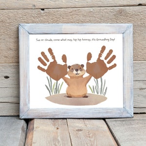 Peut inclure: Une impression d'art imprimable repr&eacute;sentant un marmotte de dessin anim&eacute; avec deux empreintes de mains au-dessus. Le texte "Sun or clouds, come what may, hip hip hooray, it's Groundhog Day!" est en haut de l'impression.