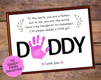 Op de afbeelding: Een wit ingelijst afdruk met een roze handafdruk en het woord "DADDY" in zwart. De afdruk bevat de tekst "To the world, you are a father, but to me, you are the world, here's my handprint to remember, I'm always daddy's little girl." en "Love you". Een roze cirkel met de tekst "TO DADDY FROM DAUGHTER" bevindt zich in de linkerbenedenhoek.