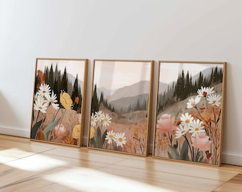 May include: Three framed art prints featuring floral and landscape scenes. The artwork includes white daisies, yellow flowers, and pink roses in a field with mountains and trees. The frames are a light brown color.