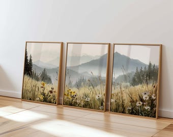 May include: Three framed landscape paintings with a misty mountain scene and wildflowers in the foreground. The paintings are in a light wood frame and are hung on a white wall.