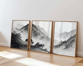 May include: Three framed black and white prints of misty mountain landscapes. The prints are in wooden frames and are arranged horizontally on a light wood floor.