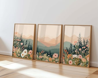 May include: Three framed prints with a mountain landscape and a field of flowers in shades of pink, orange, and green. The prints are arranged in a row on a wooden floor.