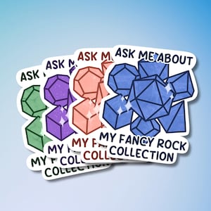 May include: A stack of colorful stickers with geometric rock illustrations. Each sticker features the text "Ask Me About My Fancy Rock Collection". The rocks are in shades of green, purple, orange, and blue, with sparkling accents. The background is a gradient of blue.