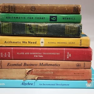 May include: A stack of vintage textbooks in various colors, including brown, green, yellow, and red. Titles visible are "Arithmetic for Today," "Plane and Spherical Trigonometry," and "Algebra." The books are worn, suggesting age and use.
