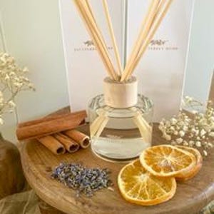 May include: A clear glass diffuser bottle with a wooden lid and natural reeds. The bottle is surrounded by dried orange slices, cinnamon sticks, and lavender flowers.