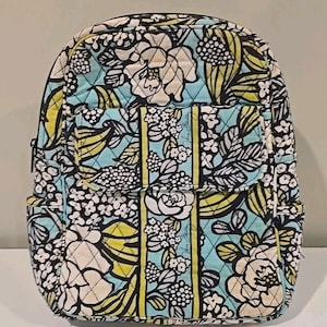 Puede incluir: Mochila con estampado floral con fondo azul claro, flores blancas y detalles amarillos. La mochila tiene múltiples bolsillos y un diseño acolchado. La bolsa tiene cierre de cremallera y es adecuada para llevar libros y otros artículos.