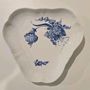 Puede incluir: Plato de cerámica blanco con una forma ondulada única y un borde texturizado. El plato está decorado con un diseño floral azul. Las flores están pintadas de manera detallada y estilizada, agregando un toque de elegancia a la pieza. Ideal para servir aperitivos o postres.