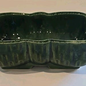 May include: A dark green ceramic planter with a scalloped rim and three distinct sections. The planter has a glossy finish and a rectangular shape, suitable for small plants or decorative items.