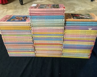 May include: A collection of The Baby-Sitters Club books, featuring various titles with colorful covers. The books are stacked in a neat arrangement, showcasing the series' branding and author, Ann M. Martin. The spines display the series title and book numbers.