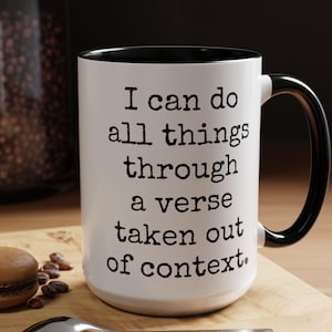 May include: White ceramic coffee mug with a black rim and handle. The mug has a black printed quote that reads "I can do all things through a verse taken out of context."