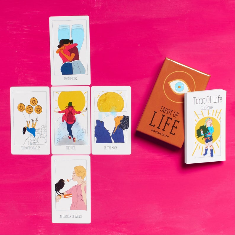 K&ouml;nnte beinhalten: Tarot of Life Deck mit 10 Karten, die auf einer rosa Oberfl&auml;che ausgelegt sind. Die Karten zeigen Illustrationen von Menschen und Symbolen. Das Handbuch ist ebenfalls auf der Oberfl&auml;che sichtbar.