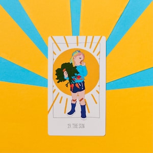 K&ouml;nnte beinhalten: Eine Tarotkarten-Illustration der Sonne-Karte, die eine Person mit Regenbogenhaaren zeigt, die einen Bund Karotten h&auml;lt und l&auml;chelt. Die Karte ist wei&szlig; mit einer gelben Sonne und Strahlen hinter der Person. Der Text "19. DIE SONNE" ist unten auf der Karte gedruckt.