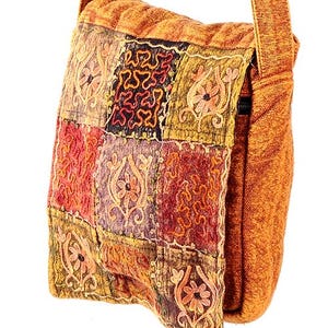 May include: Orange shoulder bag with a patchwork design on the front. The bag features a long, adjustable strap and a rectangular shape. The patchwork includes various colors and embroidered patterns. The bag is made of a textured fabric.