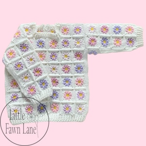 May include: White crocheted cardigan with a floral pattern in pink, purple, and yellow. The cardigan has long sleeves and a crew neckline. The text "Little Fawn Lane" is visible in the bottom left corner of the image.