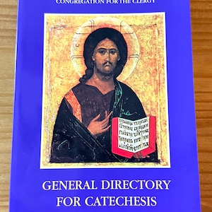 May include: A book with a blue cover featuring an icon of a religious figure. The icon is in a gold frame and depicts a man with a halo holding a red book. The text "CONGREGATION FOR THE CLERGY" and "GENERAL DIRECTORY FOR CATECHESIS" are printed on the cover.