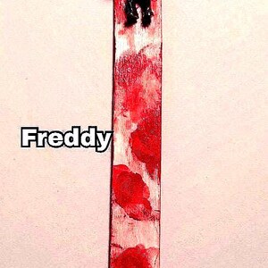 includes : A Freddy Krueger bookmark features a small figurine of the horror movie character affixed to a painted bloody bookmark. The bookmark is predominantly white with red blood splatter paint accents. The figurine is approximately 2 inches tall and depicts Freddy Krueger in his signature attire: a red and green striped sweater, brown fedora, and glove with blades. The bookmark measures approximately 8 inches in length. great horror fan gift. bookmark very as they are hand painted.