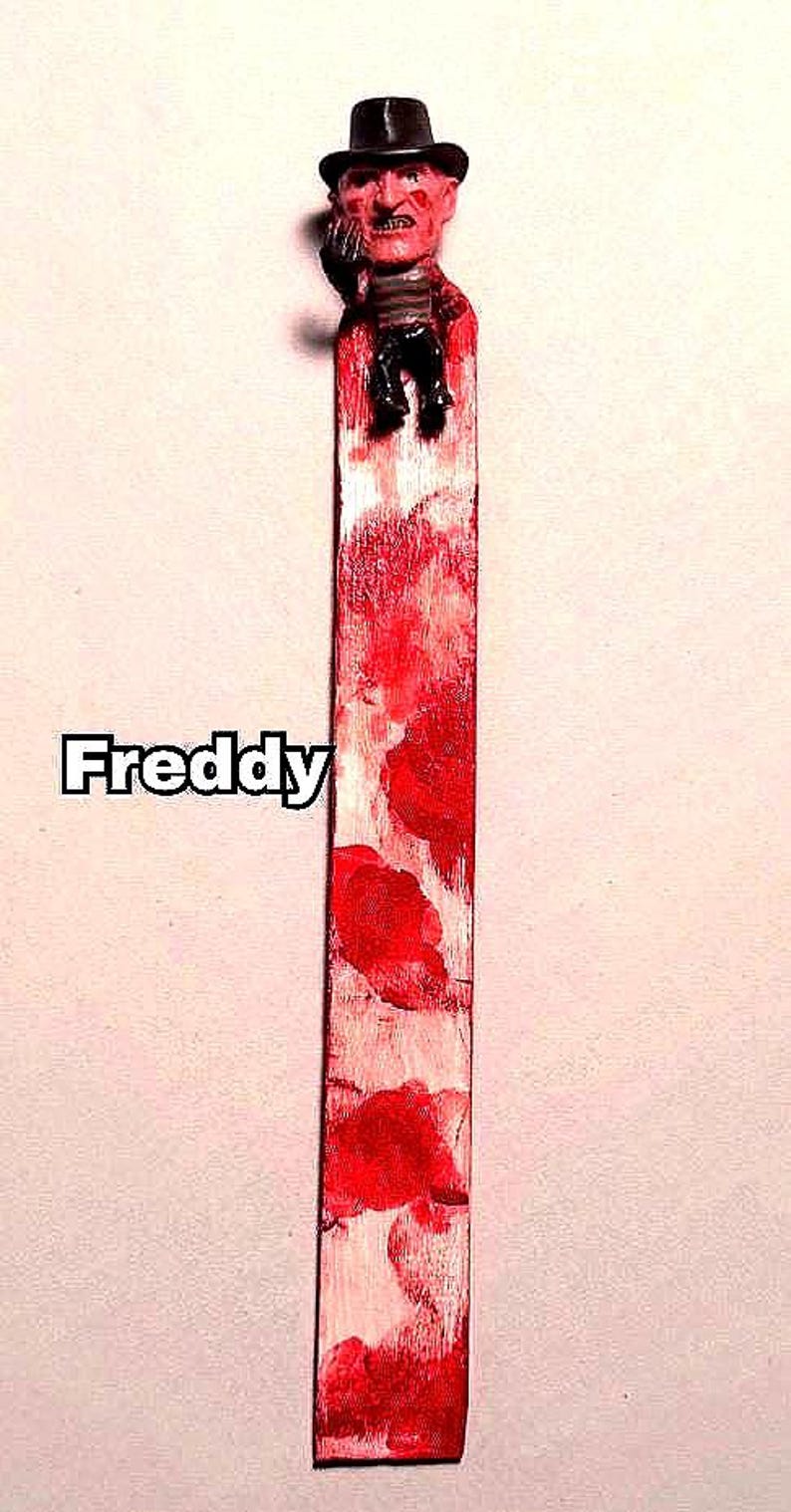 includes : A Freddy Krueger bookmark features a small figurine of the horror movie character affixed to a painted bloody bookmark. The bookmark is predominantly white with red blood splatter paint accents. The figurine is approximately 2 inches tall and depicts Freddy Krueger in his signature attire: a red and green striped sweater, brown fedora, and glove with blades. The bookmark measures approximately 8 inches in length. great horror fan gift. bookmark very as they are hand painted.