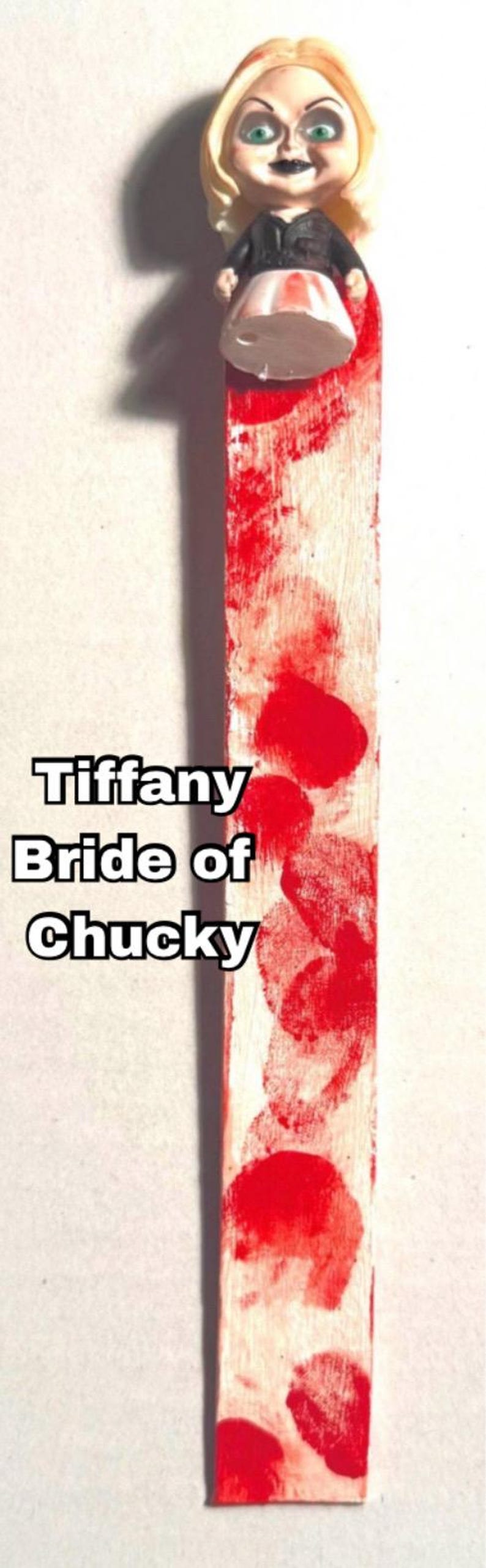 includes: A handmade bookmark features a small Tiffany Bride of Chucky doll figurine on top of a long, rectangular bookmark painted white with red splatter paint, resembling blood. The bookmark measures approximately 8 inches in length.  Tiffany Bride of Chucky is a popular horror movie character great Halloween gift!