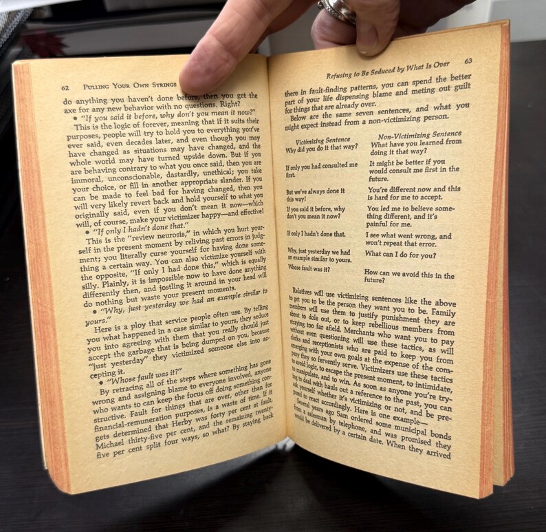 May include: Open book with text on pages 62 and 63. The text discusses victimizing sentences and how to avoid them. The pages are yellowed with age, suggesting an older publication. The book is open, with a hand visible.