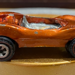 Peut inclure: Une voiture jouet vintage orange en métal moulé sous pression avec des pneus noirs et des jantes argentées. La voiture classique a un design élégant à toit ouvert et montre des signes d'usure.
