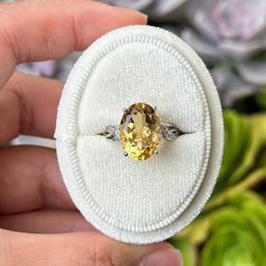 May include: A gold oval-shaped gemstone ring with a twisted band set in a white metal. The ring is displayed in a white velvet ring box.