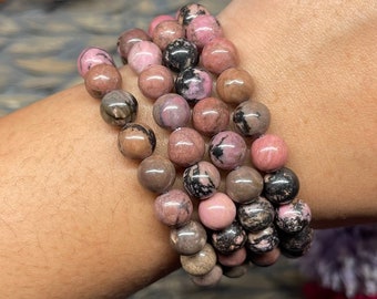 May include: A stack of pink and black gemstone bracelets. The bracelets are made of round beads and are worn on a person's wrist.