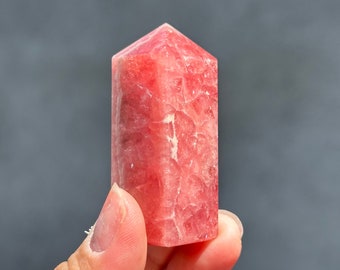 May include: A pink crystal point with a smooth, polished surface. The crystal is a light pink color and has a pointed tip.