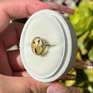 Op de afbeelding: Een zilveren ring met een gele ovale barnsteen in een bezel setting. De barnsteen heeft kleine bruine insluitsels.