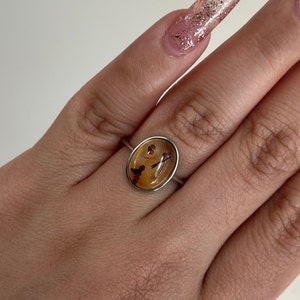 Op de afbeelding: Een zilveren ring met een bruine, ovale steen in het midden. De steen heeft een uniek patroon van bruine en zwarte insluitsels.