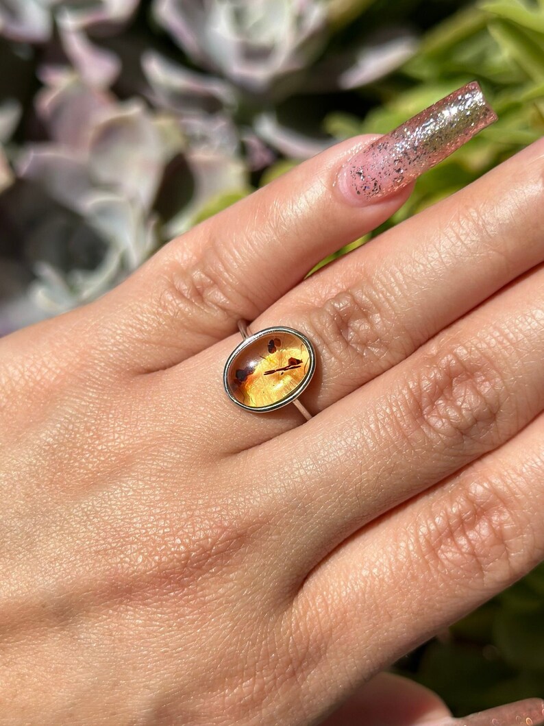 Op de afbeelding: Een zilveren ring met een gele ovale amber steen gezet in een bezel setting.
