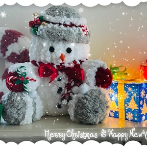 Peut inclure: Un bonhomme de neige en peluche avec un chapeau gris, une écharpe rouge et des mitaines est entouré de cadeaux emballés. Le bonhomme de neige tient un sucre d'orge et est à côté de cadeaux bleus, rouges et verts. Le texte "Merry Christmas & Happy New Year" est en bas.