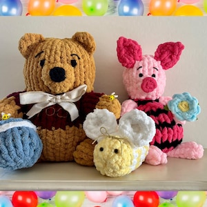 May include: Crocheted Winnie the Pooh, Piglet, and a bee. Winnie the Pooh is tan with a red shirt and a white bow. Piglet is pink with a black and pink striped shirt. The bee is yellow and white. A blue ball is in the image.