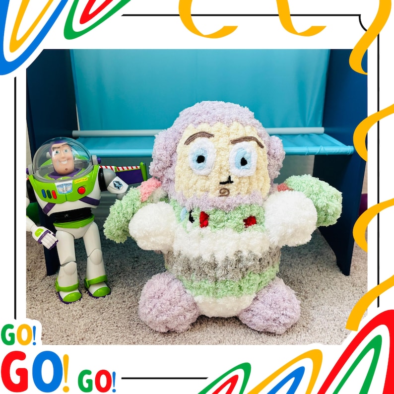 May include: A handmade, plush Buzz Lightyear doll with a light purple head, green arms, and a white and green body. A Buzz Lightyear action figure stands to the left. The word "GO!" is written in red and green.