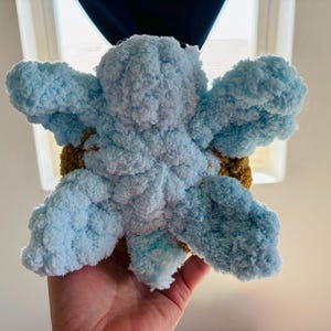 May include: A handmade, plush, blue and brown crocheted flower. The flower has large, fluffy petals in shades of light blue, with a brown center. The soft texture and vibrant colors make it a charming decorative item.