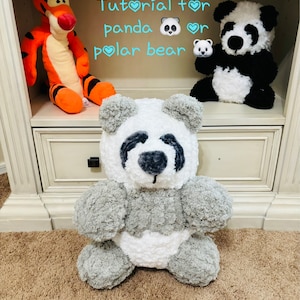 May include: Tutorial for panda or polar bear plush toy. The image shows a gray and white panda plush toy sitting on a brown carpet. The panda has black eyes and a black nose. The panda is sitting on a shelf with other plush toys.